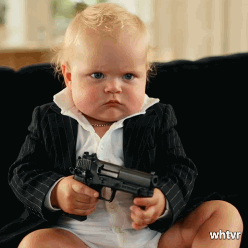 A cute little baby holding a handgun looking like a little gangster